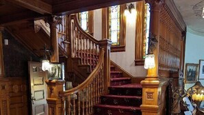 Una imponente escalera con barandales de madera decorados y un suelo cubierto de alfombra roja.