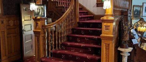 Una imponente escalera con barandales de madera decorados y un suelo cubierto de alfombra roja.