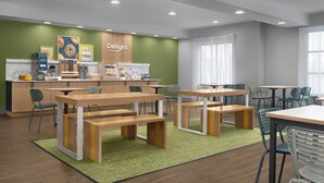Un café moderno con mesas y sillas de madera, un mostrador con una exhibición de yogur y una pared de acento verde.