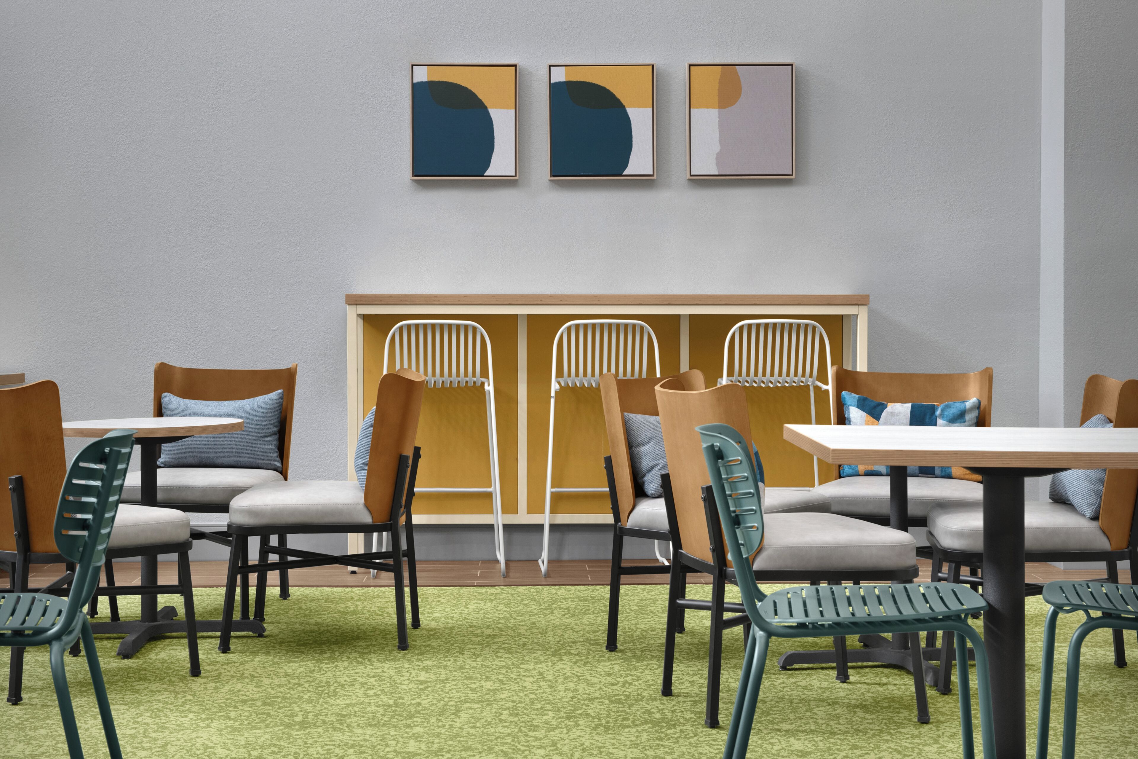 Un área de descanso con mesas y sillas, alfombra verde y arte abstracto en la pared.