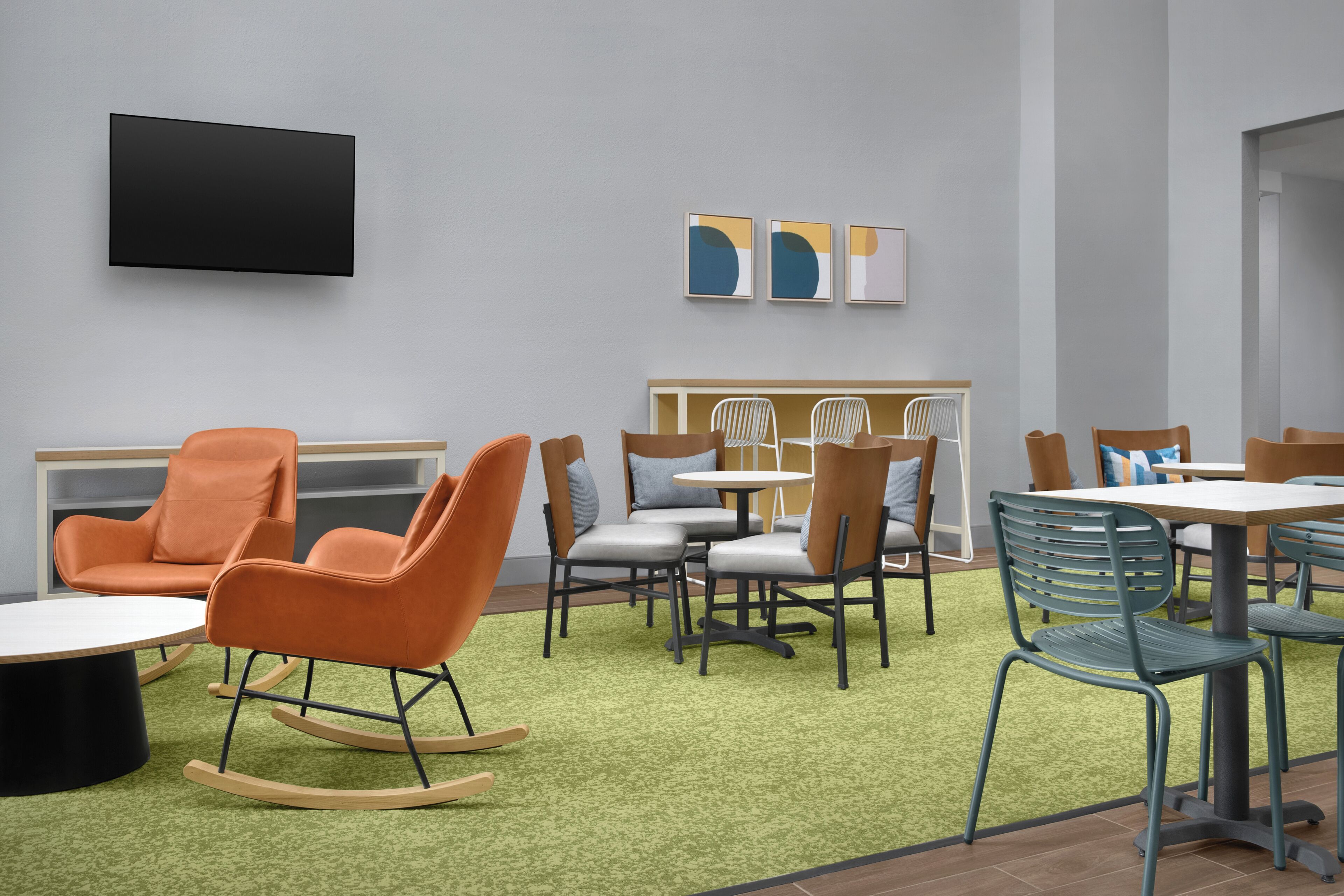 A modern interior with a flat-screen TV, abstract wall art, and a mix of seating options including chairs and a rocking chair.