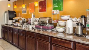 A hotel breakfast buffet with various food items, a coffee station, and a refrigerator.