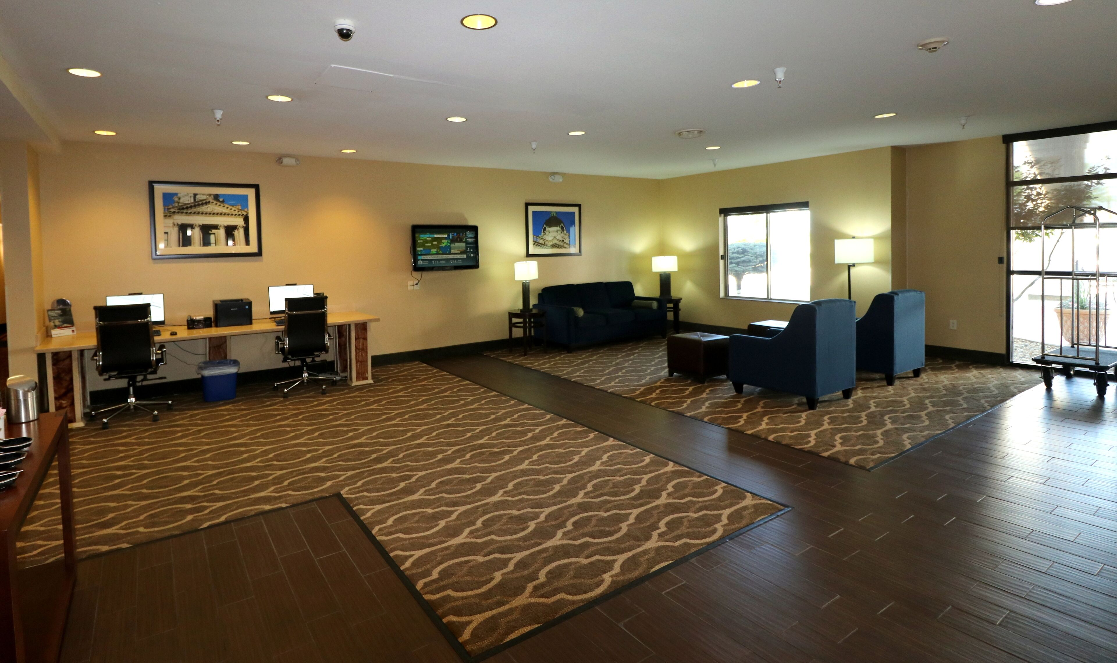 A spacious hotel lobby with a reception desk, computers, seating area, and large windows offering a view.