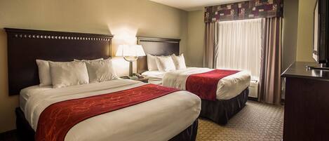 A hotel room with two beds, each with a red and white bedspread, a nightstand with a lamp, a dresser, and a television.