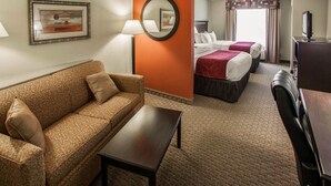 A hotel room with a sofa, a small table, two beds with red and white bedding, a TV, and a mirror on the wall.