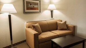 A hotel room with a patterned sofa, two floor lamps, a framed picture on the wall, and a small table.