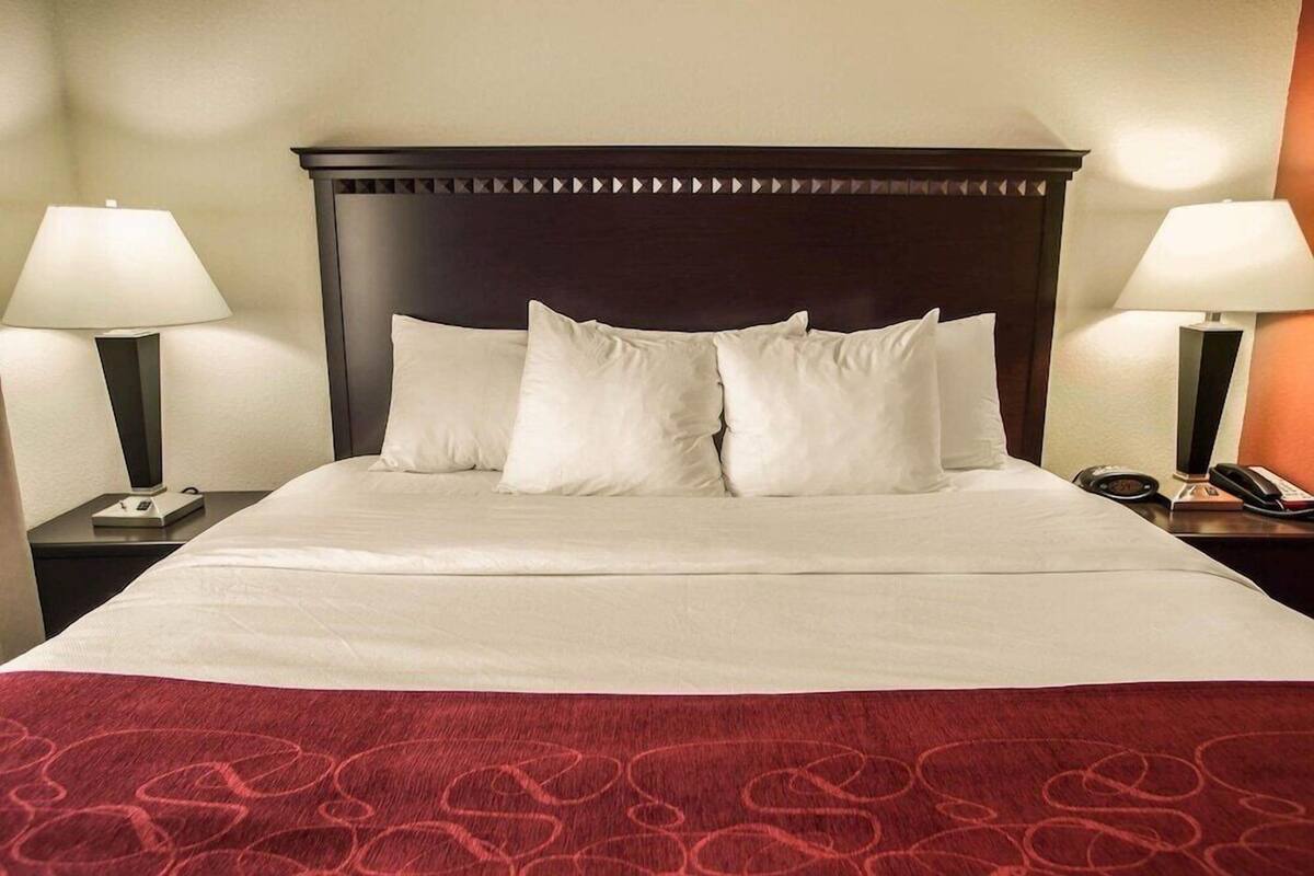 Una habitación de hotel con una cama grande, dos mesitas de noche con lámparas, y un plaid rojo estampado.