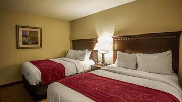 A hotel room with two beds, a nightstand with a lamp, a framed picture on the wall, and a carpeted floor.