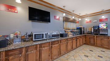 A kitchen area with a granite countertop, wooden cabinets, a microwave, a coffee machine, and a television mounted on the wall.