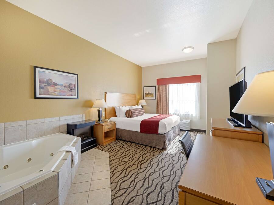 A hotel room with a large bathtub, a bed with a red blanket, a television, and a painting on the wall.