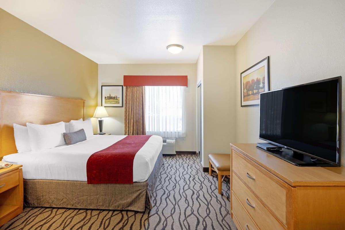 Quarto de hotel com cama, televisão, secretária e cadeira.