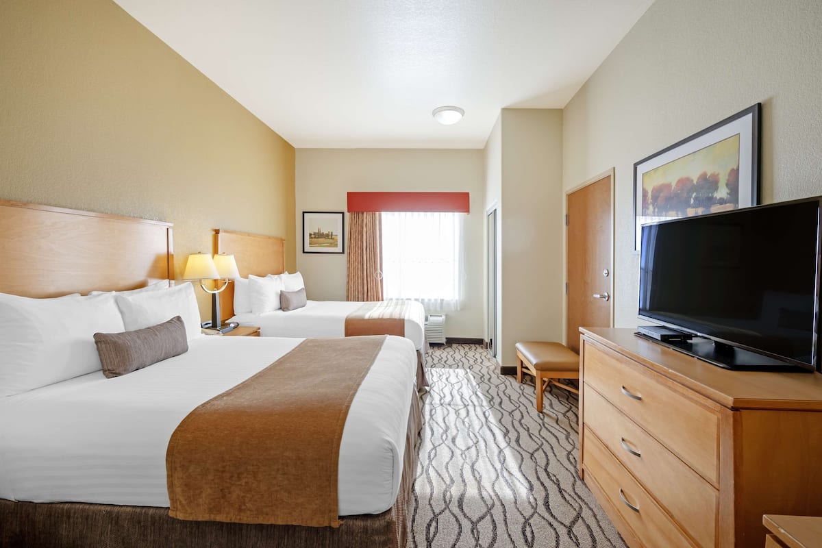 Quarto de hotel com duas camas, televisão, cômoda e janela com cortinas.