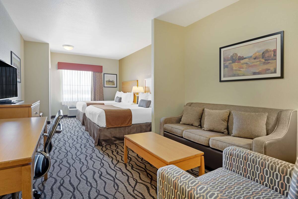 Quarto de hotel com cama, sofá, escrivaninha e televisão.