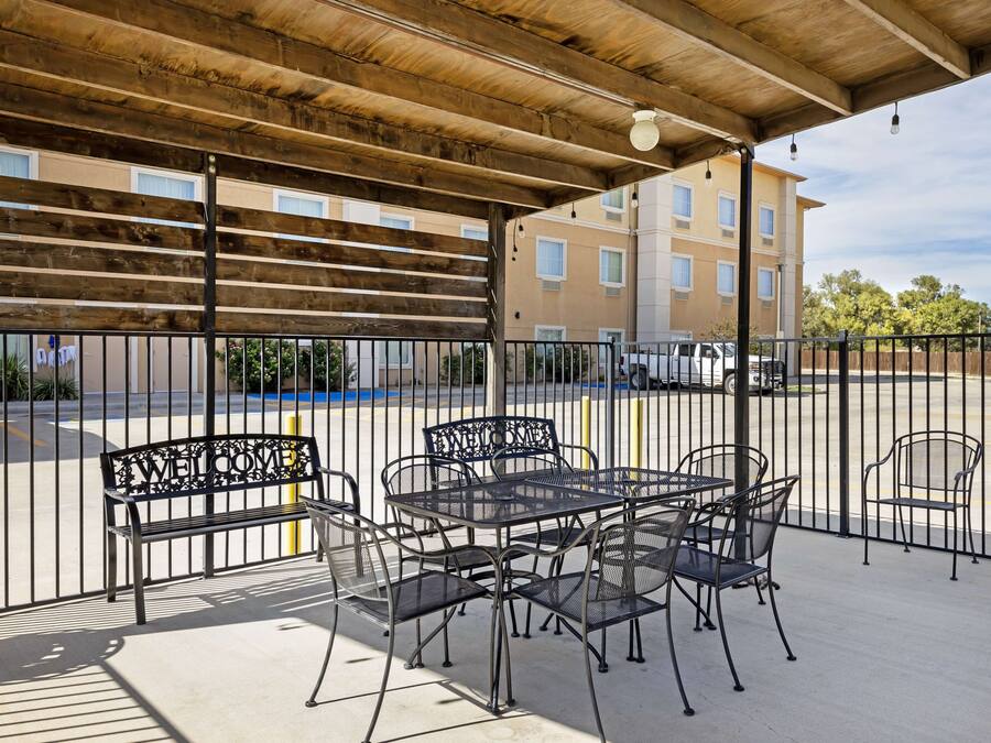 An outdoor patio with a covered seating area, a metal fence, and a view of a parking lot and buildings in the background.