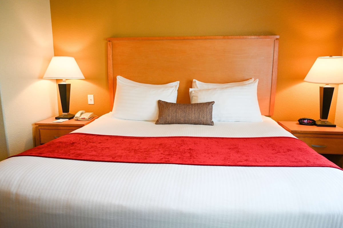Quarto de hotel com uma cama grande, duas mesas de cabeceira, um cobertor vermelho e duas luminárias.