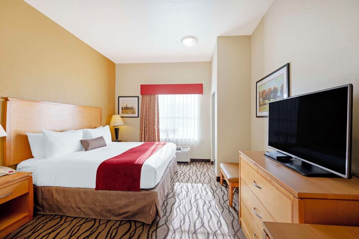 Habitación de hotel con cama, televisión, escritorio y ventana con cortinas.