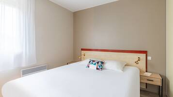 A hotel room with a large bed, a bedside table, a nightstand, and a window with curtains.