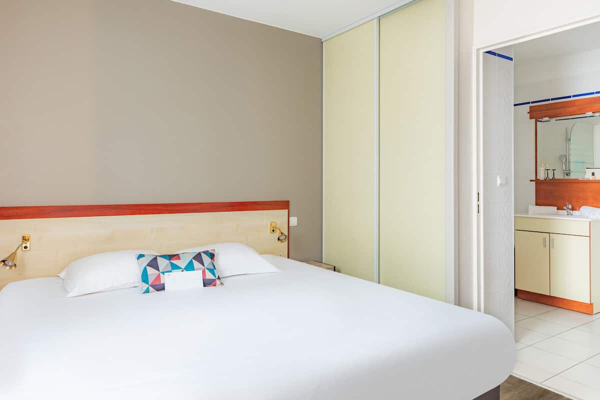 Une chambre d’hôtel avec un grand lit, une tête de lit en bois, une salle de bain avec un miroir et un lavabo.