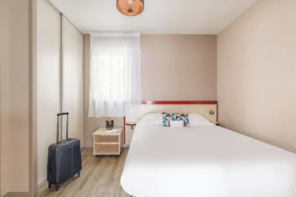 A hotel room with a large bed, a suitcase, a nightstand, and a window with curtains.