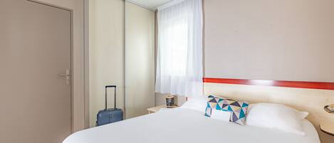 A hotel room with a large bed, a suitcase, a nightstand, and a window with curtains.