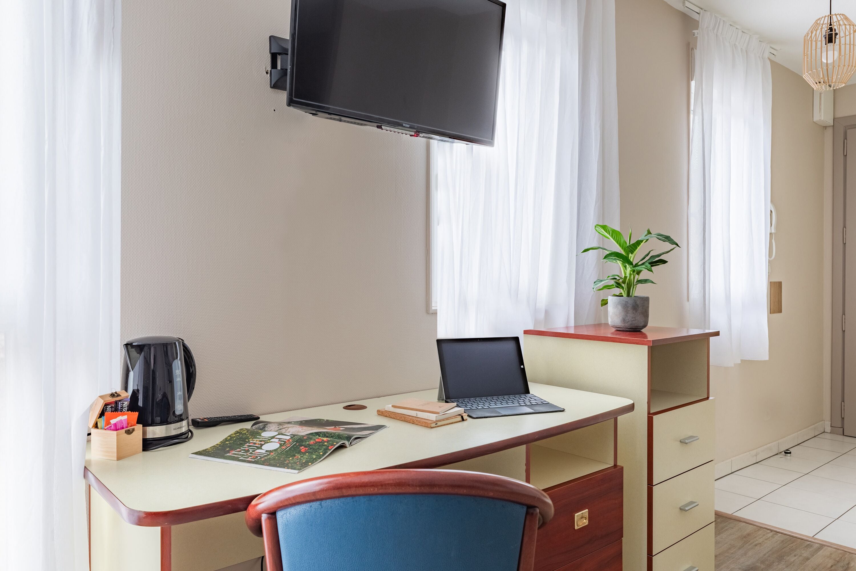 Ein Hotelzimmer mit Schreibtisch, Laptop, Kaffeemaschine und einer Zimmerpflanze.
