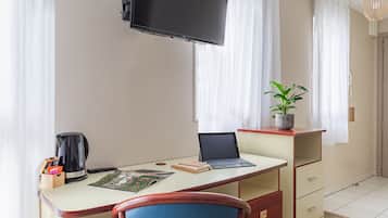 Habitación de hotel con escritorio, ordenador portátil, cafetera y planta en maceta.
