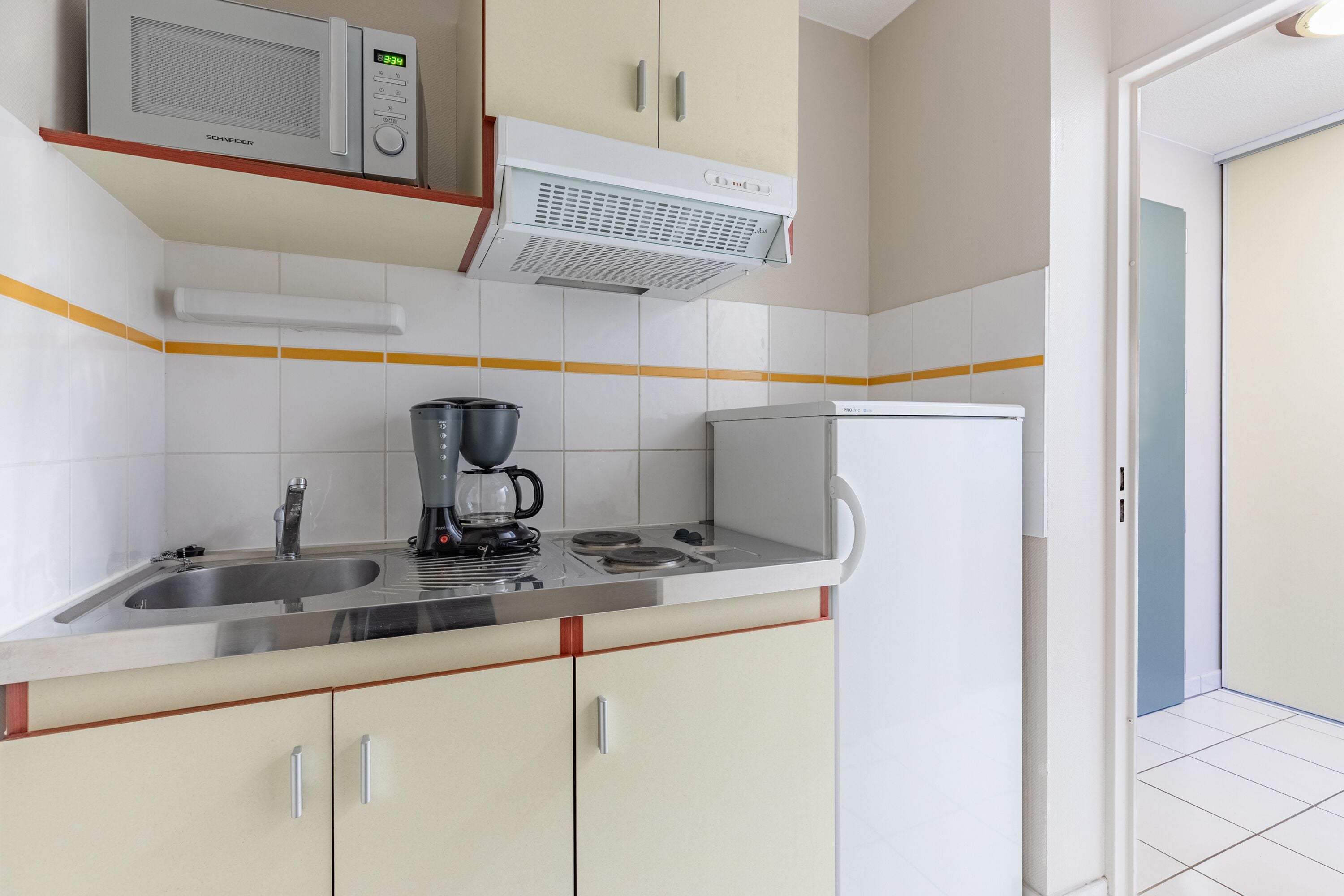 Een keuken met een magnetron, koffiezetapparaat en een koelkast.