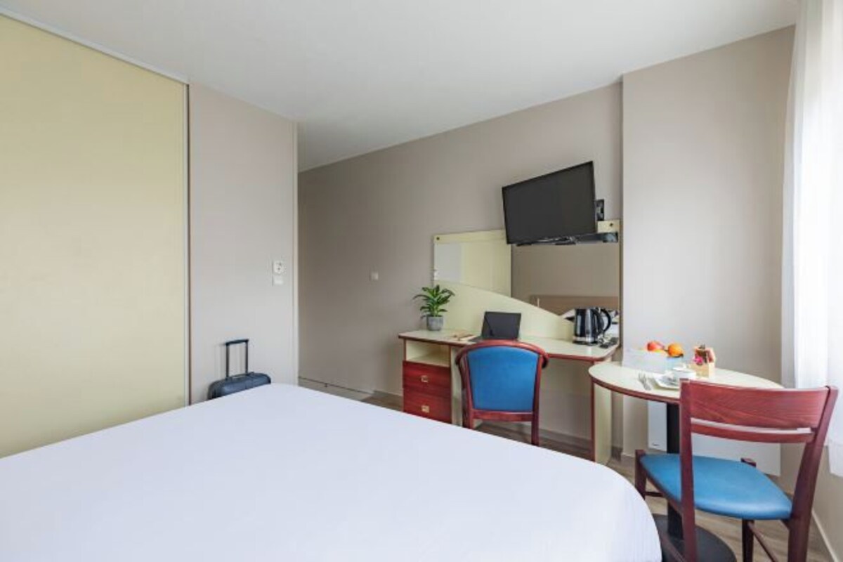 A hotel room with a bed, desk, chair, and a television on the wall.