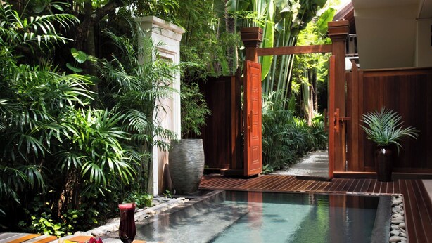 A serene pool area surrounded by lush greenery, wooden deck, and a stone pathway leading to a wooden gate. - Anantara Angkor Resort (Siem Reap)