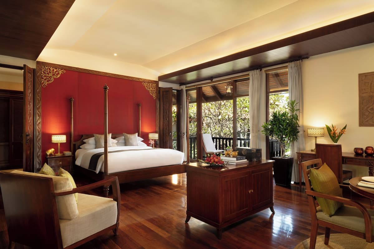 A bedroom with a large bed, a desk, a chair, and a balcony with plants.