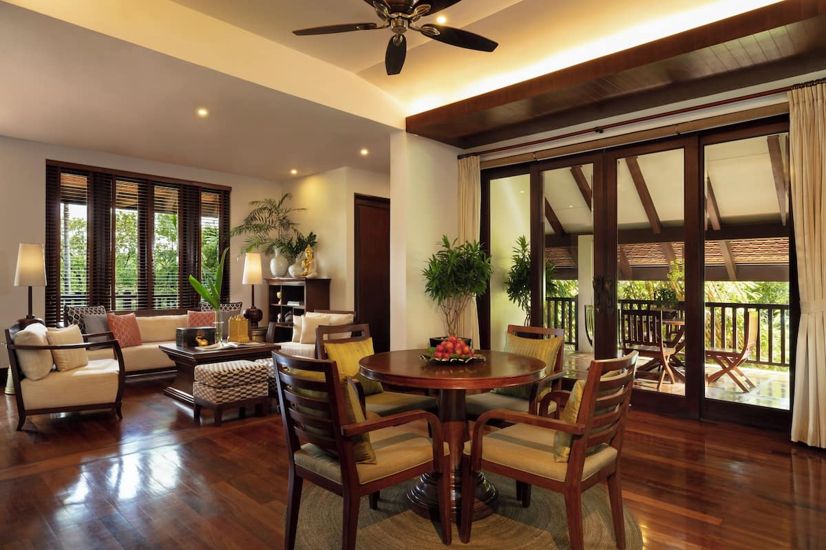 A spacious living room with a wooden floor, a ceiling fan, a sofa, a coffee table, and a dining area with chairs and a table.