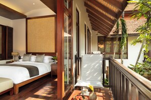Relax in this serene bedroom with a large bed, nightstand, and comfortable chair, offering a balcony with a view of lush surroundings.