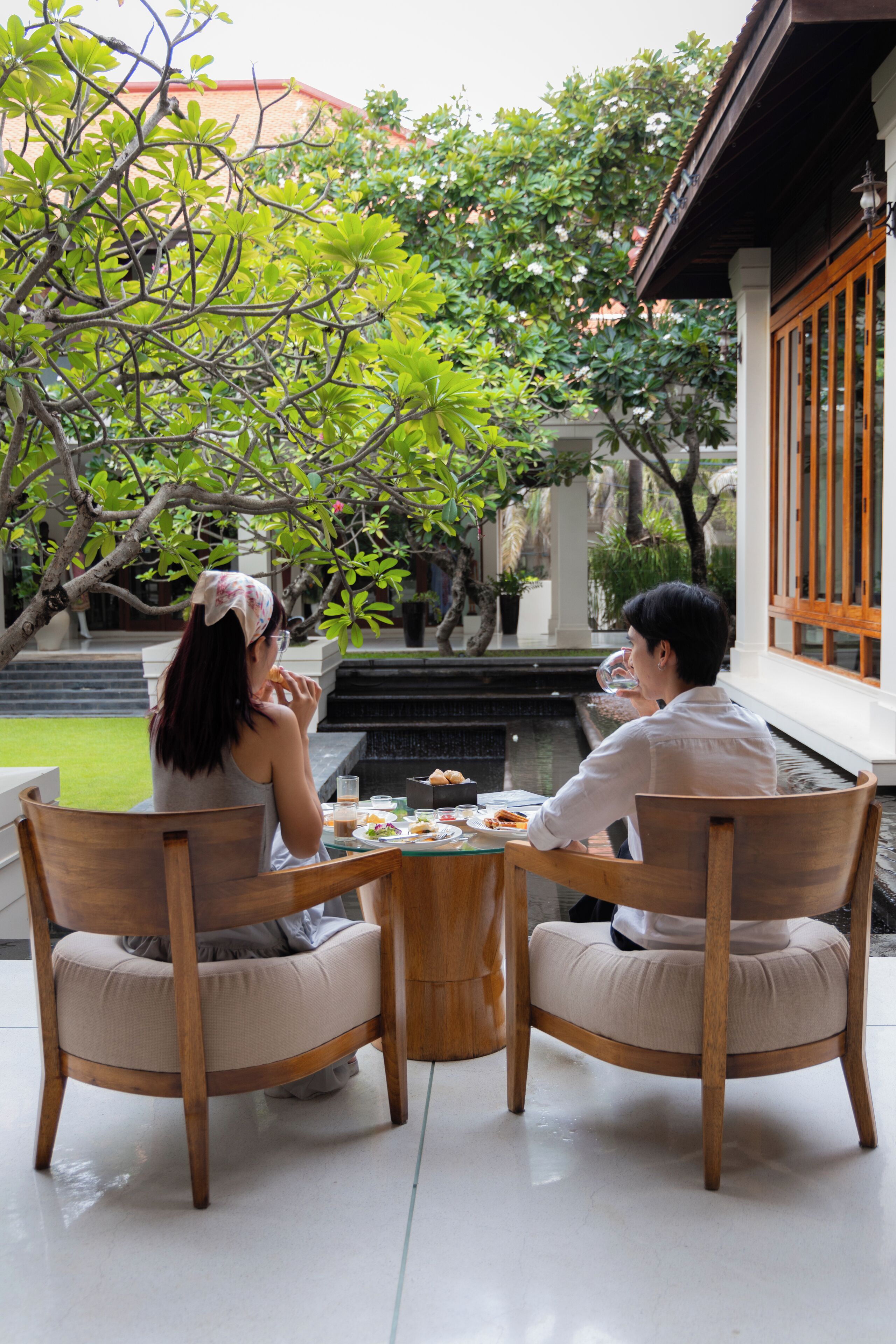Dos personas cenando en una mesa con vistas a un jardín y un estanque.