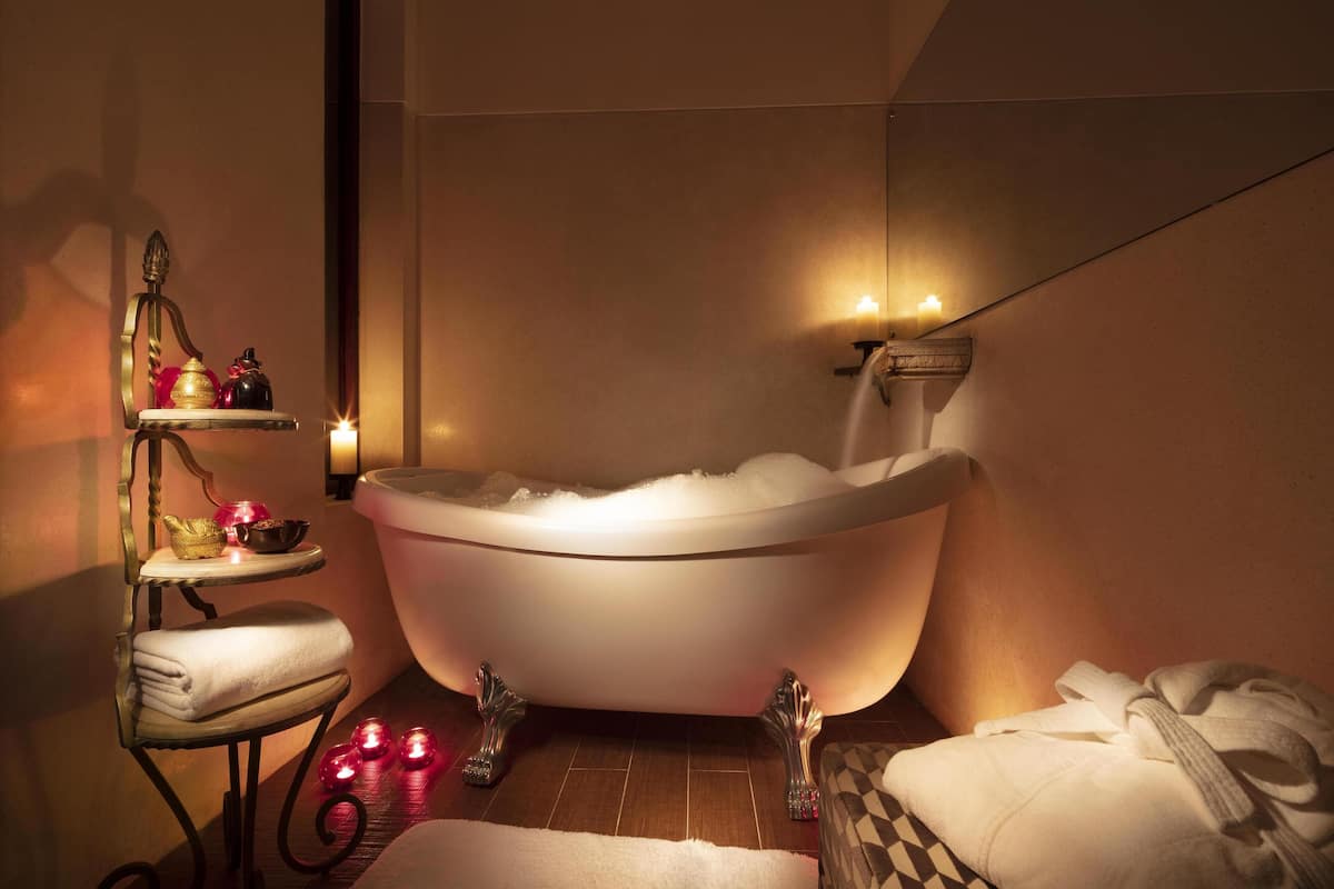 A modern bathroom with a freestanding bathtub, a small vanity with a mirror, and a shelf with toiletries.