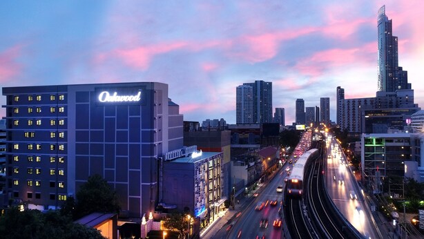 A high-rise hotel with a prominent sign, a busy highway, and a city skyline with modern buildings. - Oakwood Hotel & Residence Bangkok (Bangkok)