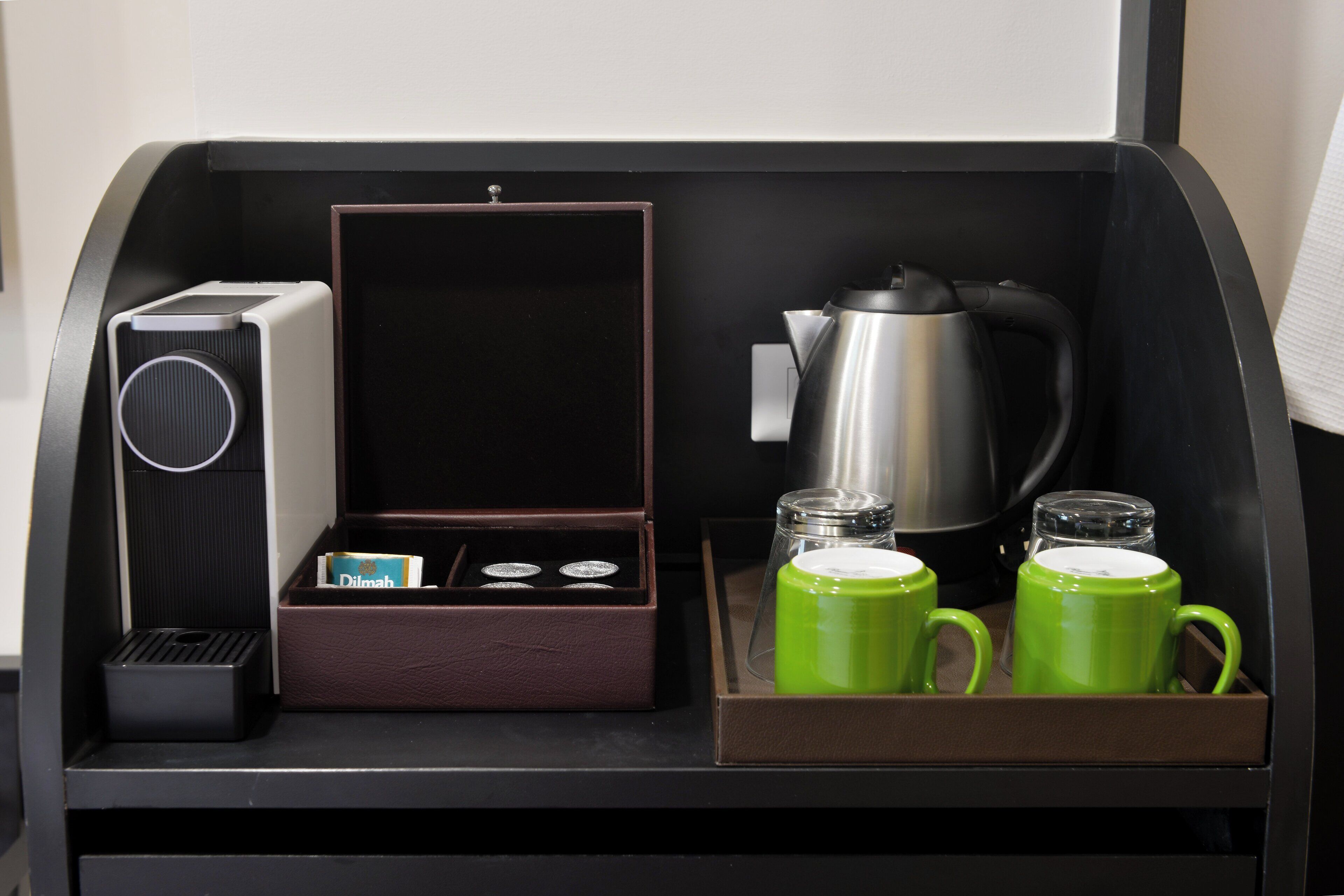 Un coin café équipé d’une machine à café, d’une boîte de thé et de deux tasses vertes.