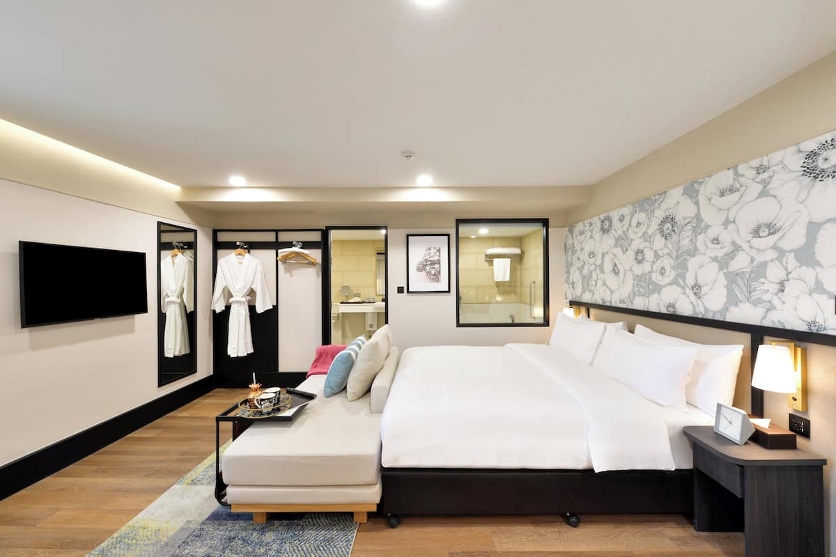 Une chambre d’hôtel moderne avec un grand lit, un canapé, une télévision et un miroir.