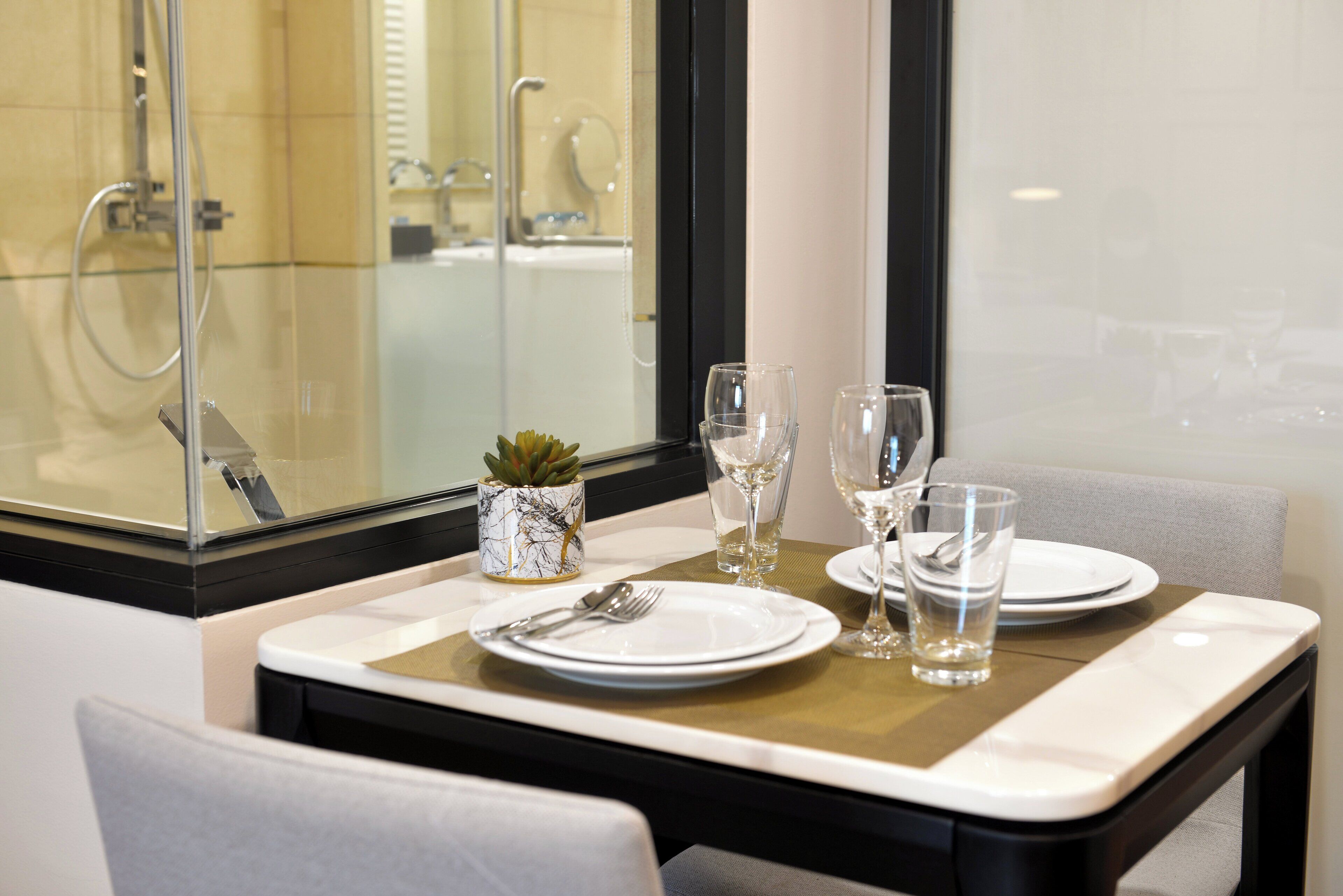 A dining table set with plates, cutlery, and glasses, with a small plant and a glass vase.