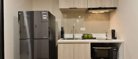 Una cocina compacta con un refrigerador de acero inoxidable, un microondas y armarios de madera clara.