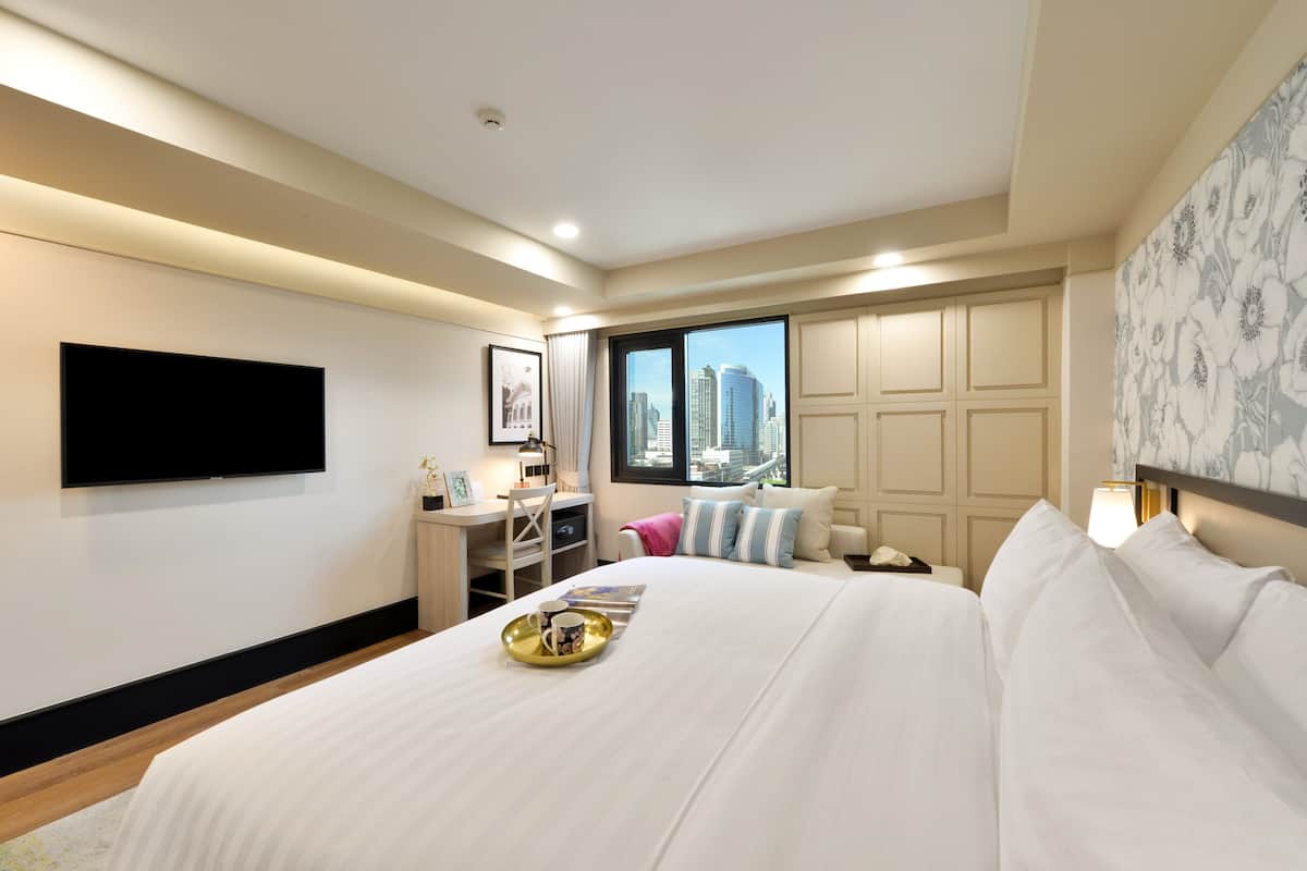 Une chambre d’hôtel avec un grand lit, un bureau, une chaise, un téléviseur à écran plat et une fenêtre donnant sur la ville.