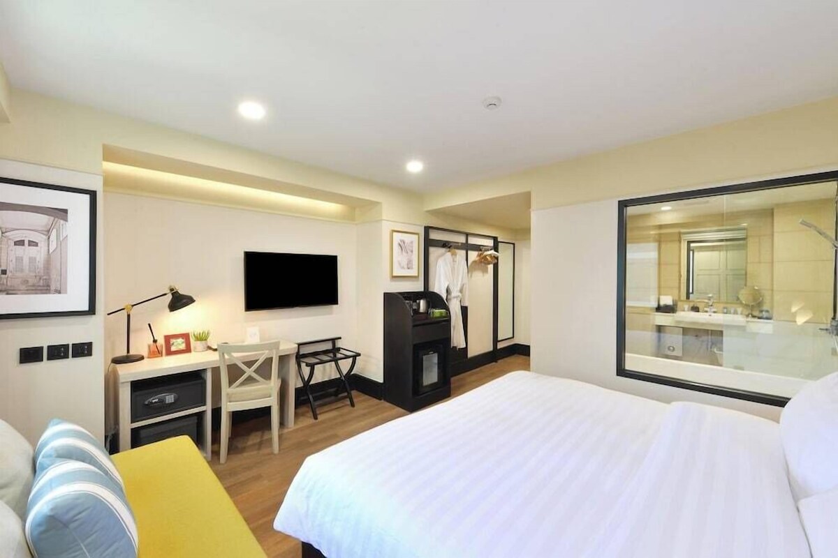 A hotel room with a bed, desk, chair, TV, and a large mirror.