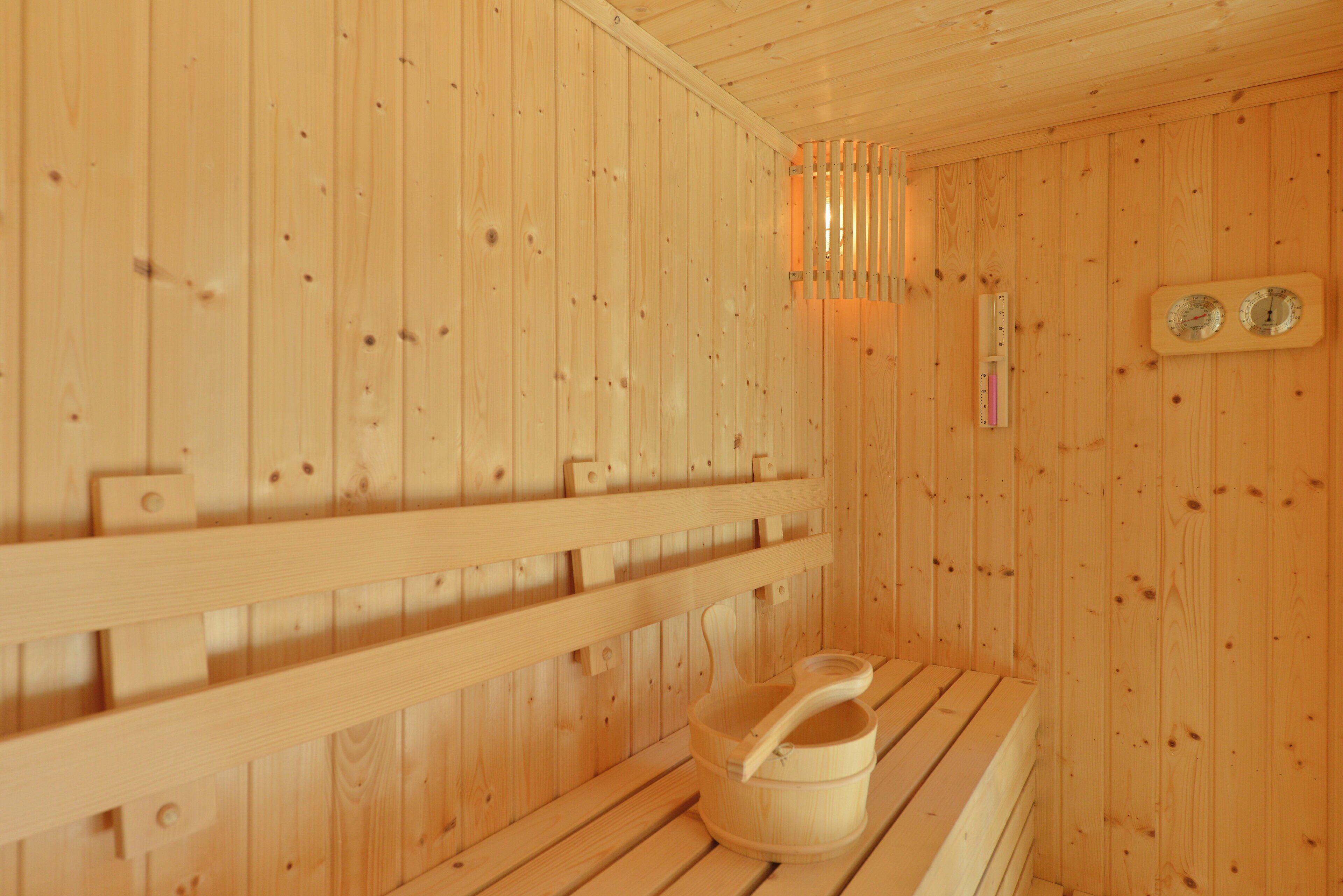 A wooden sauna with a bench, a wooden bucket, and two wall-mounted thermometers.