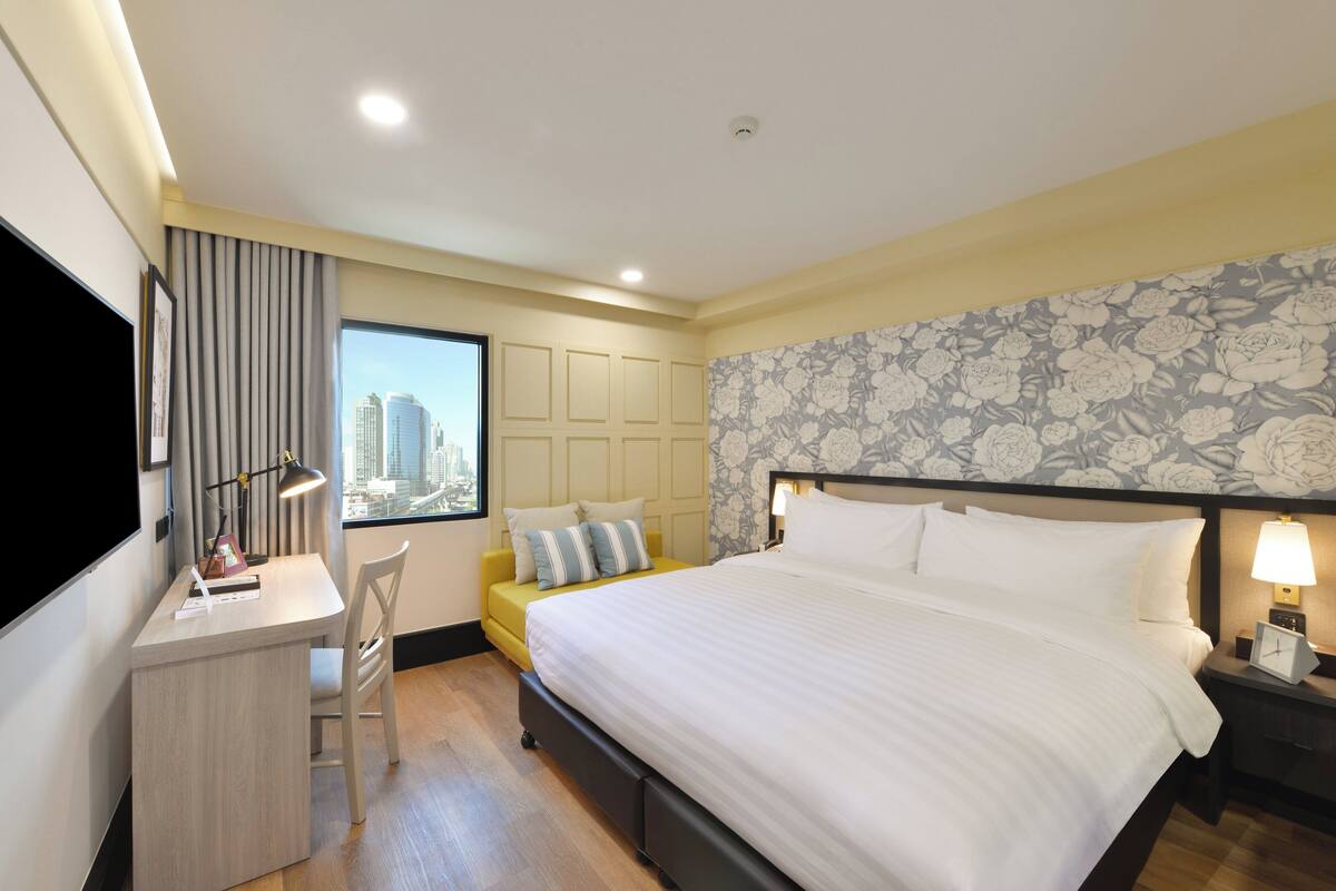 Une chambre d’hôtel équipée d’un lit, d’un bureau, d’une chaise et d’une fenêtre donnant sur la ville.