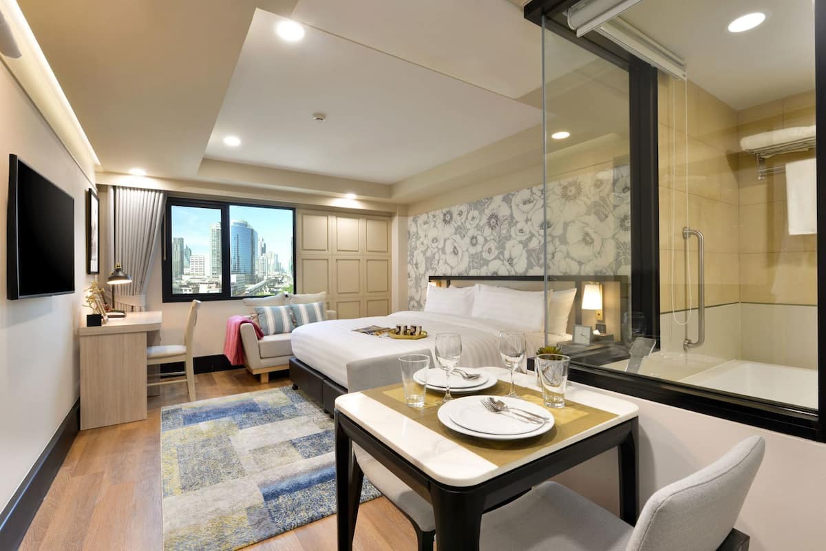 Une chambre d’hôtel comprenant un lit, un bureau, une table à manger dressée avec des assiettes et des verres, une douche et une vue sur la ville.