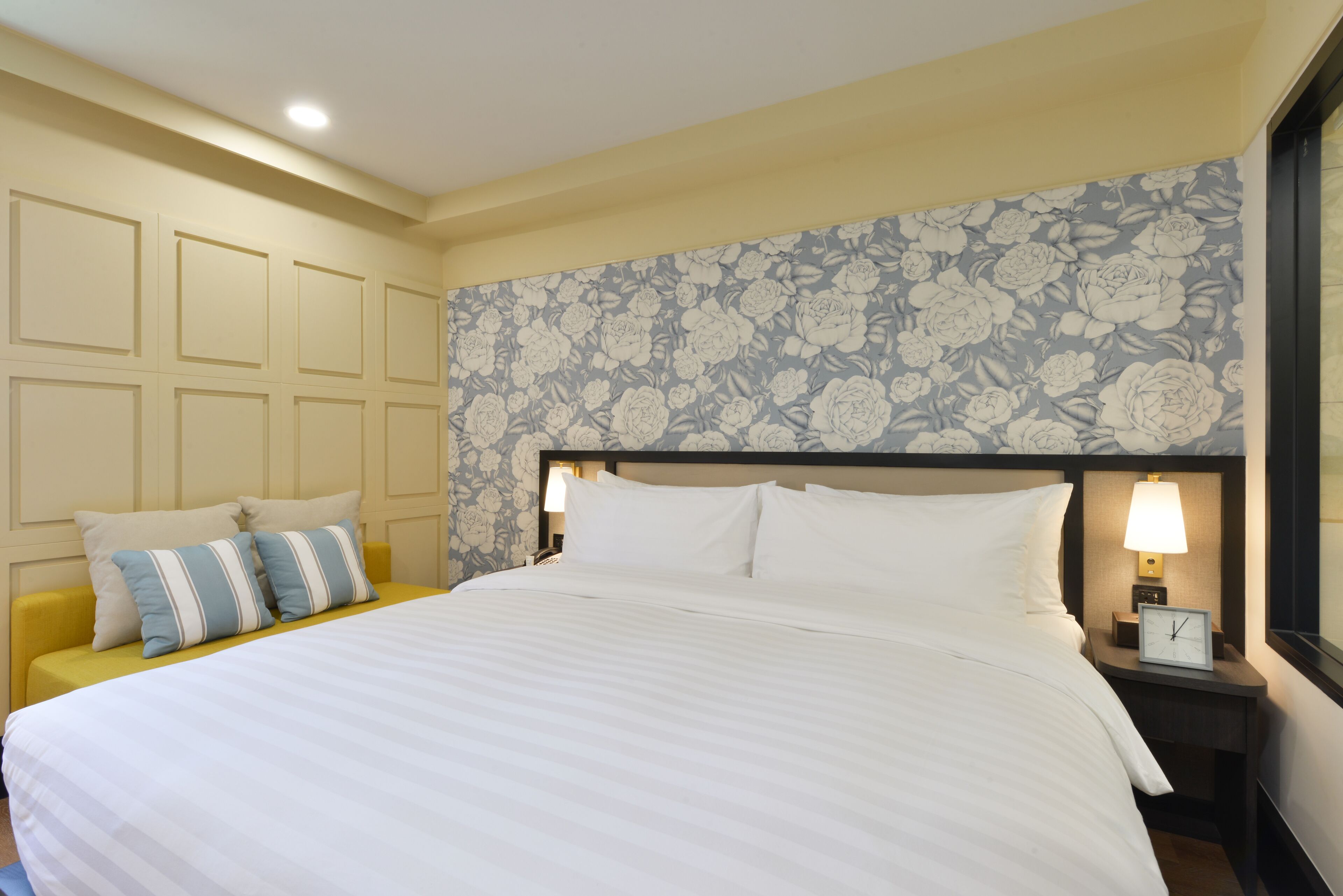 Habitación de hotel con una cama grande, una mesita de noche con lámpara y un papel tapiz con estampado floral.