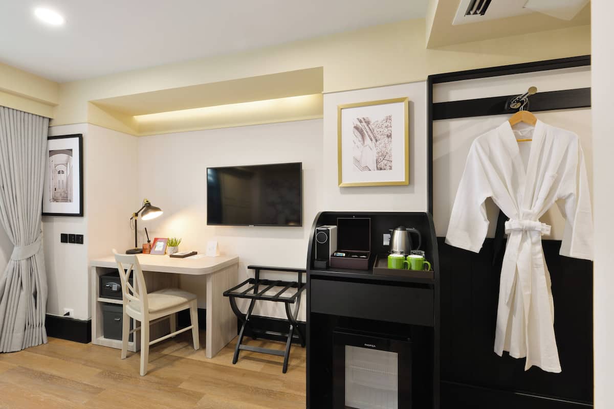 Une chambre d’hôtel équipée d’un bureau, d’une chaise, d’un téléviseur à écran plat, d’une kitchenette et d’un peignoir accroché au mur.