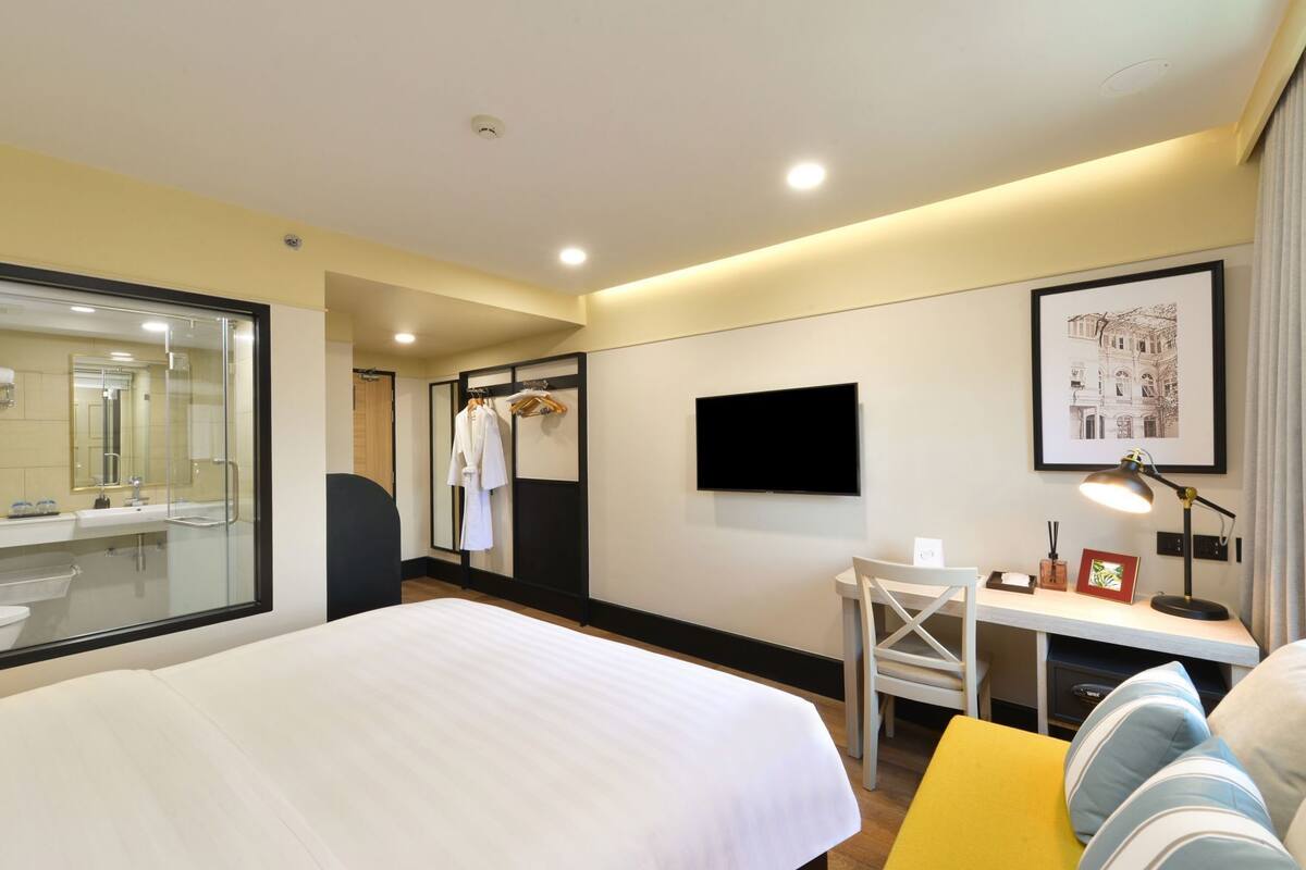 Une chambre d'hôtel comprenant un lit, un bureau, une chaise, une télévision et une salle de bain avec une douche à parois de verre.