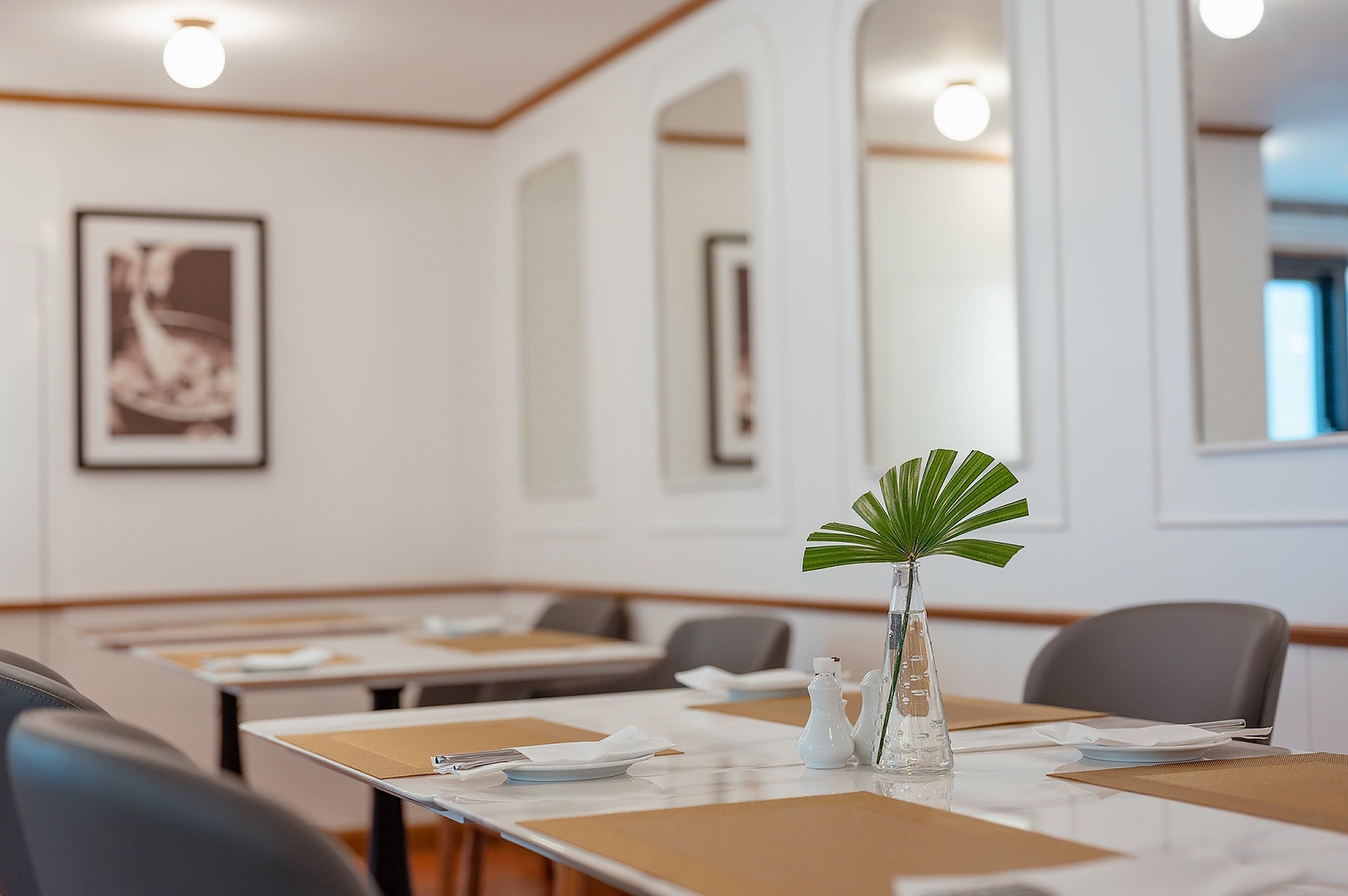 A conference room with tables set for meetings, a vase with a plant, and framed artwork on the wall.