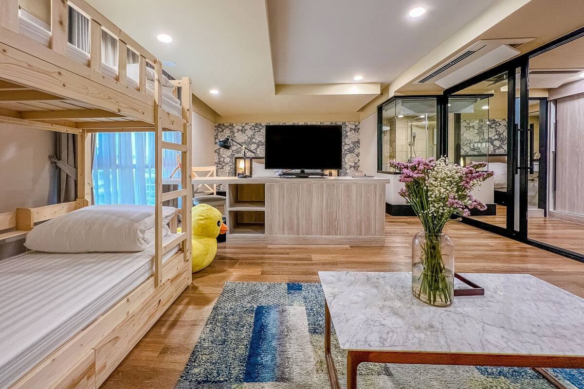 Une chambre avec des lits superposés, un bureau, une télévision et un vase de fleurs.