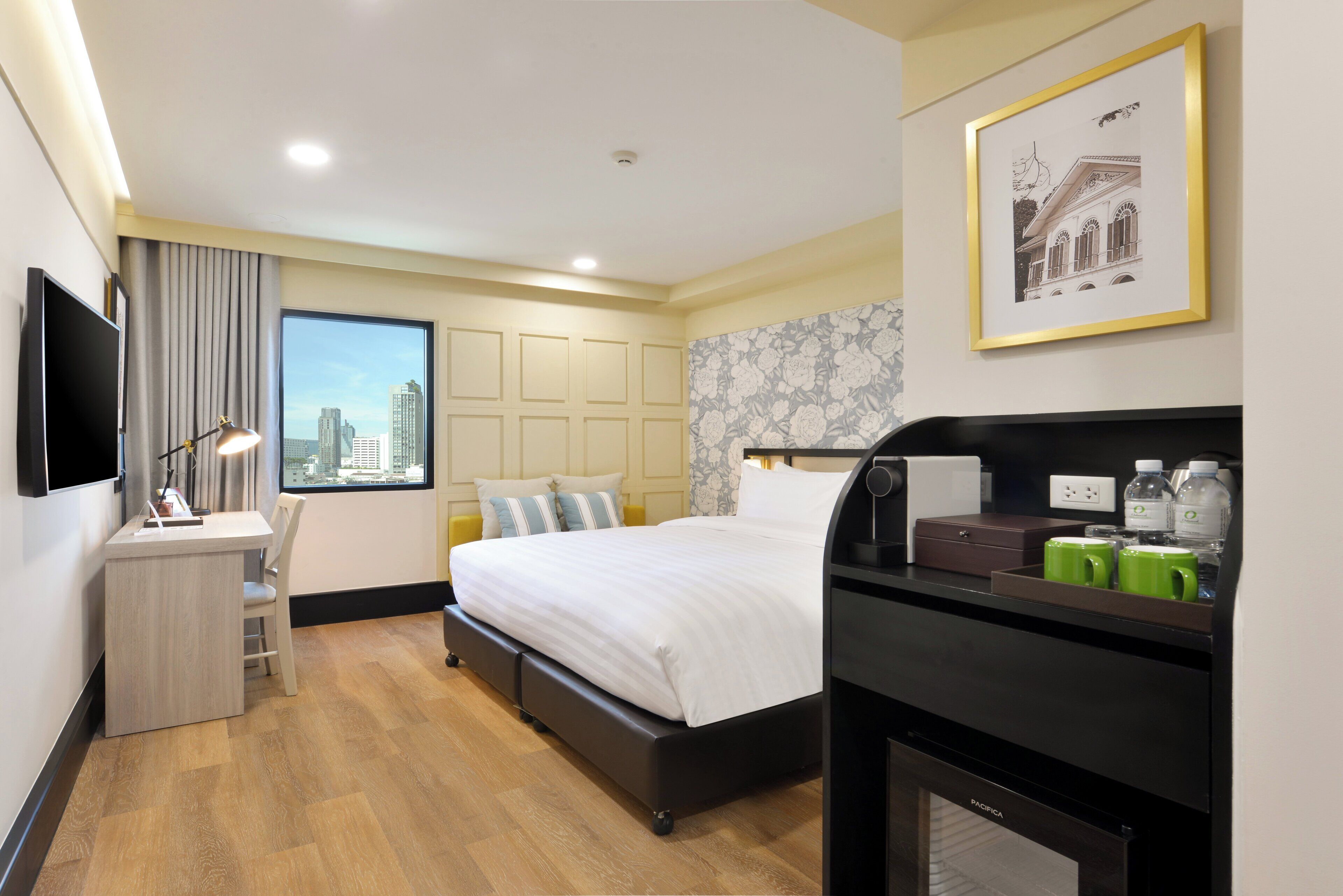 A hotel room with a bed, desk, chair, and a view of the city.